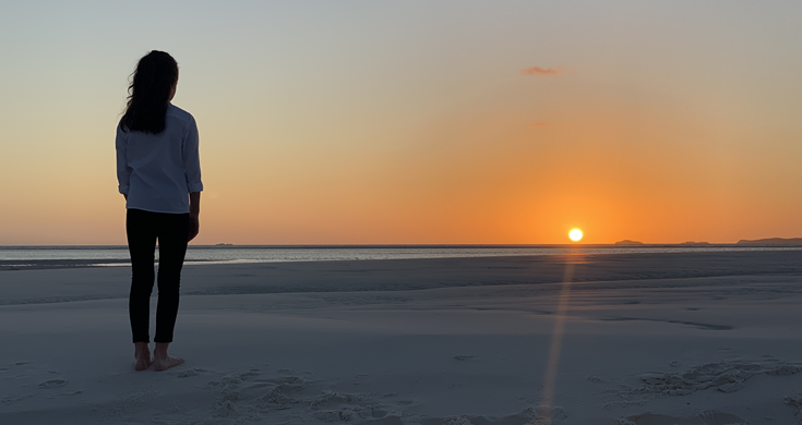 Lily wearing Qantas choir white shirt and black pants watching the sunrise at Whitehaven beach.