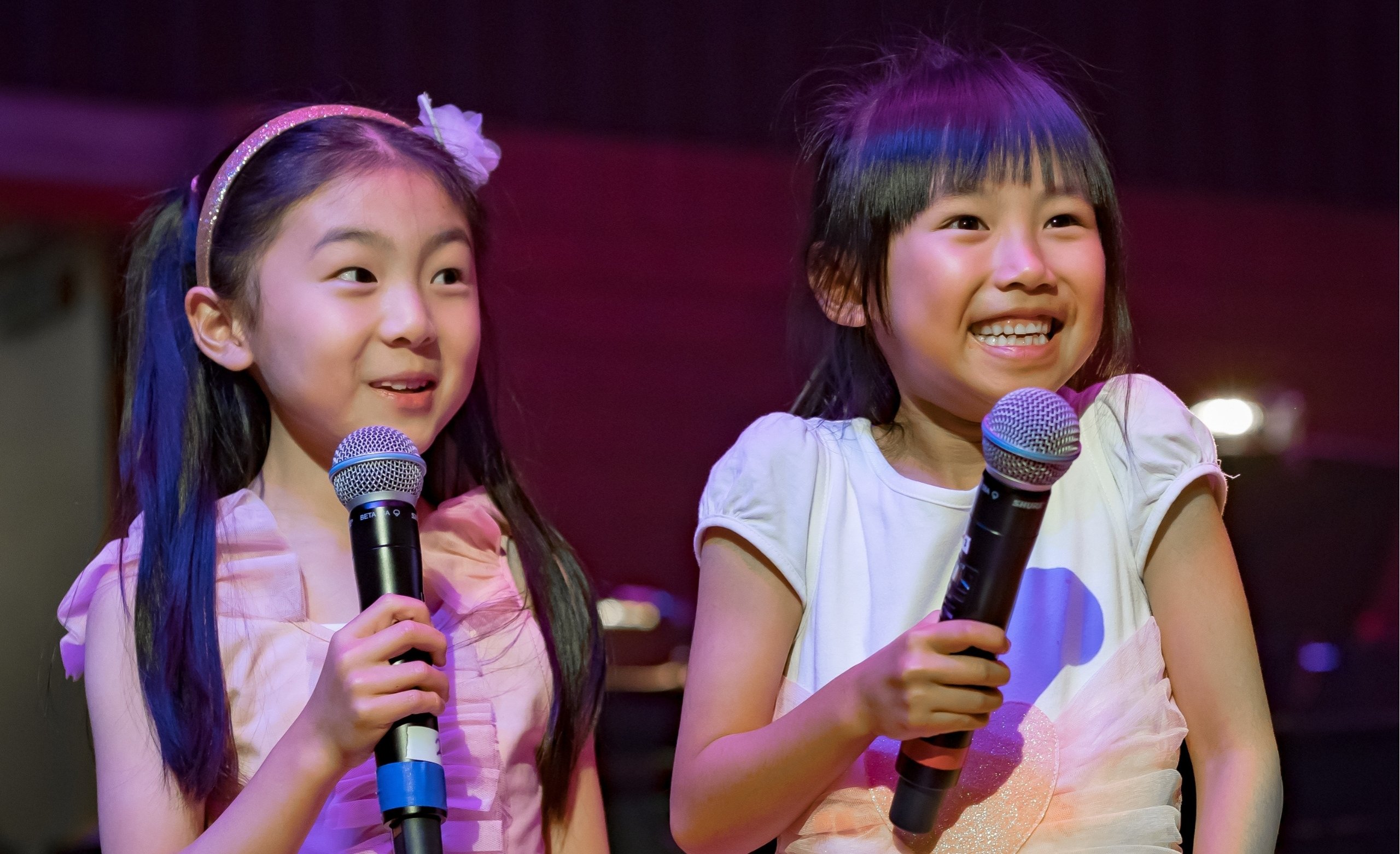 two girls smiling with microphones on stage