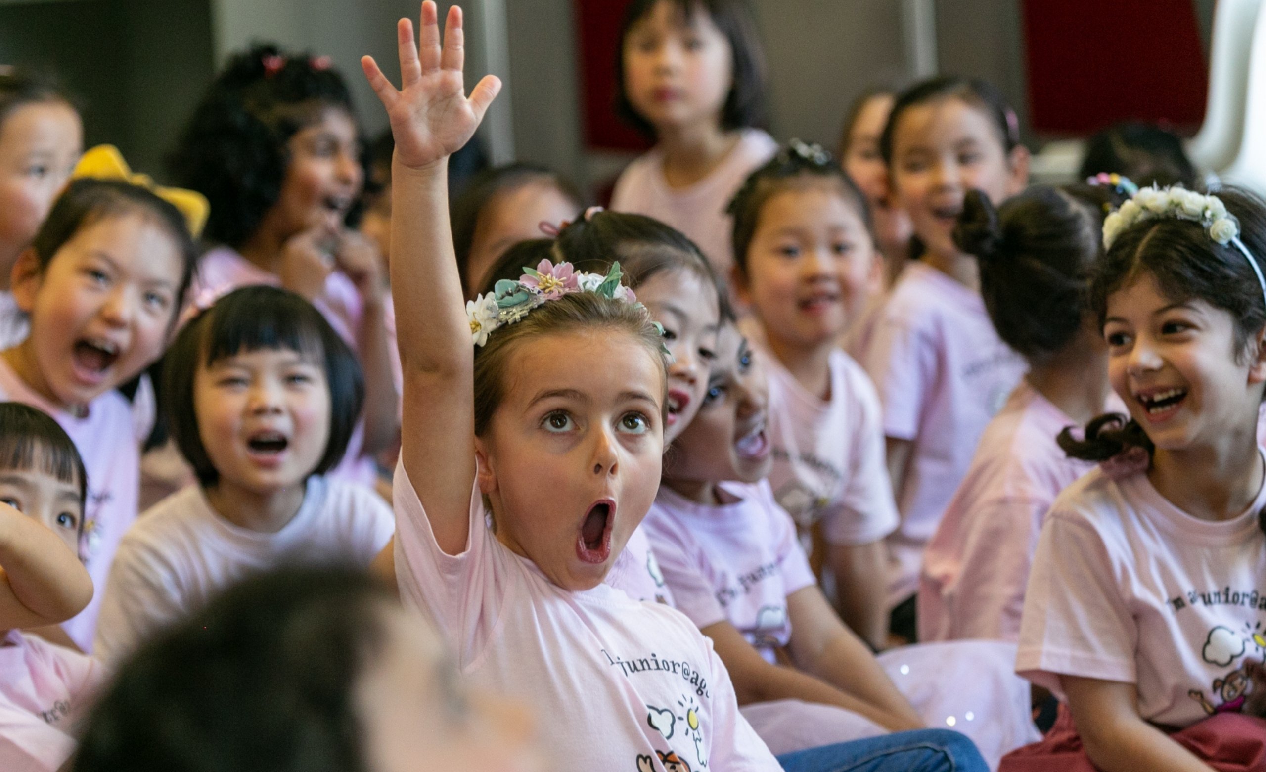 young girl in class with hand up wearing pink shirt