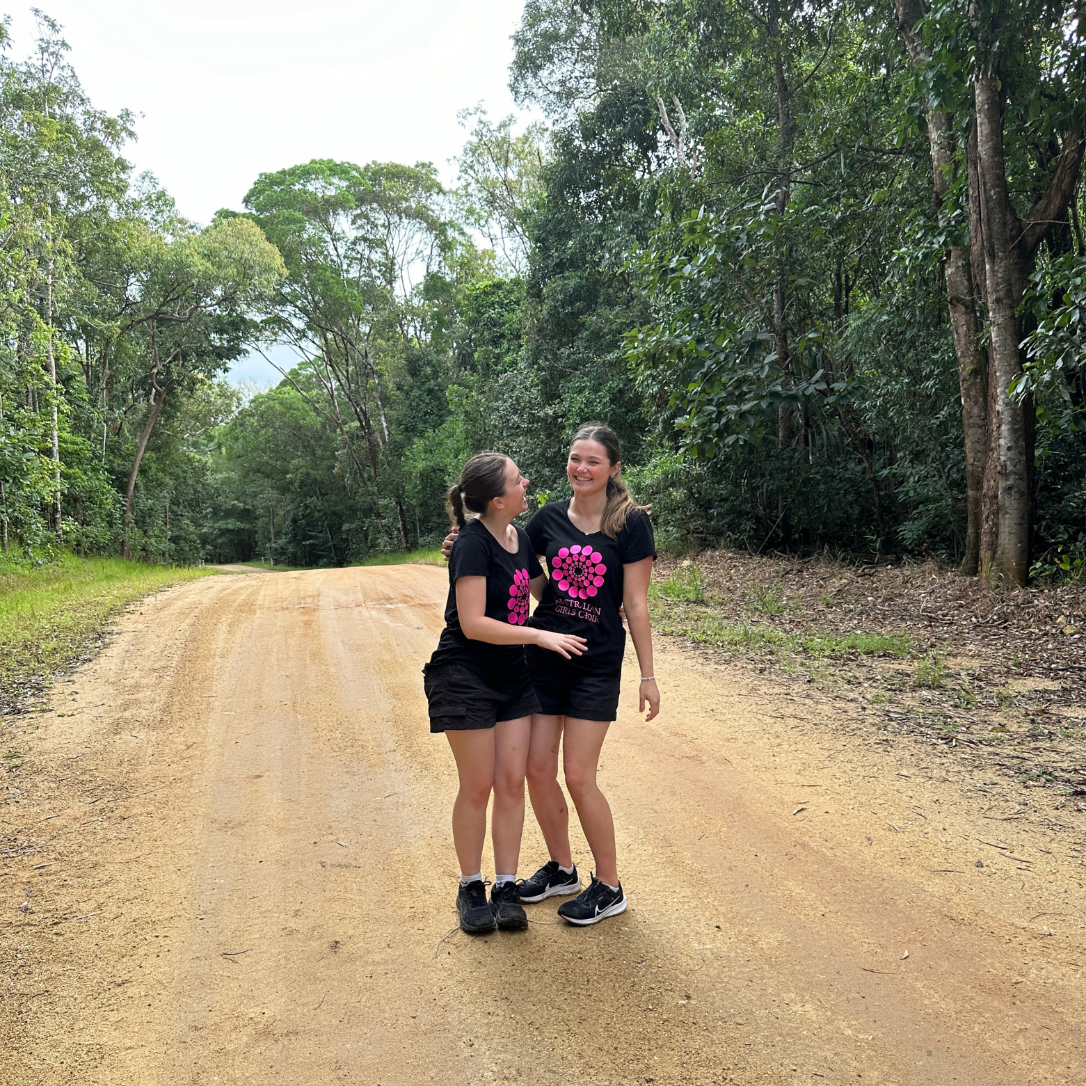 Two AGC choristers stand together laughing on a clearing in the rainforest