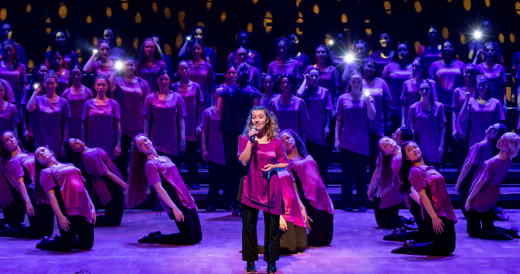 AGC choristers perform on stage in a group with beautiful purple lighting