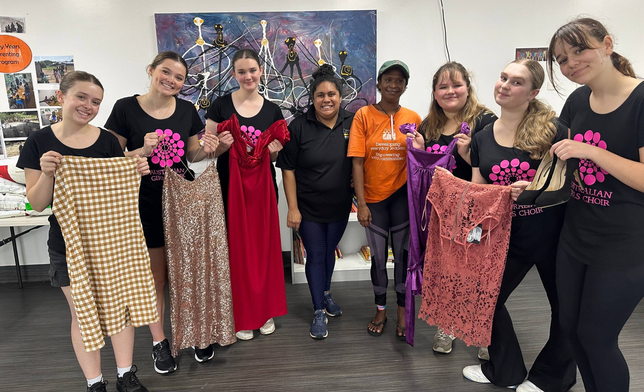 AGC choristers visit the Puuya Foundation to donate dresses to the NAIDOC ball. They are pictured holding up the dresses.