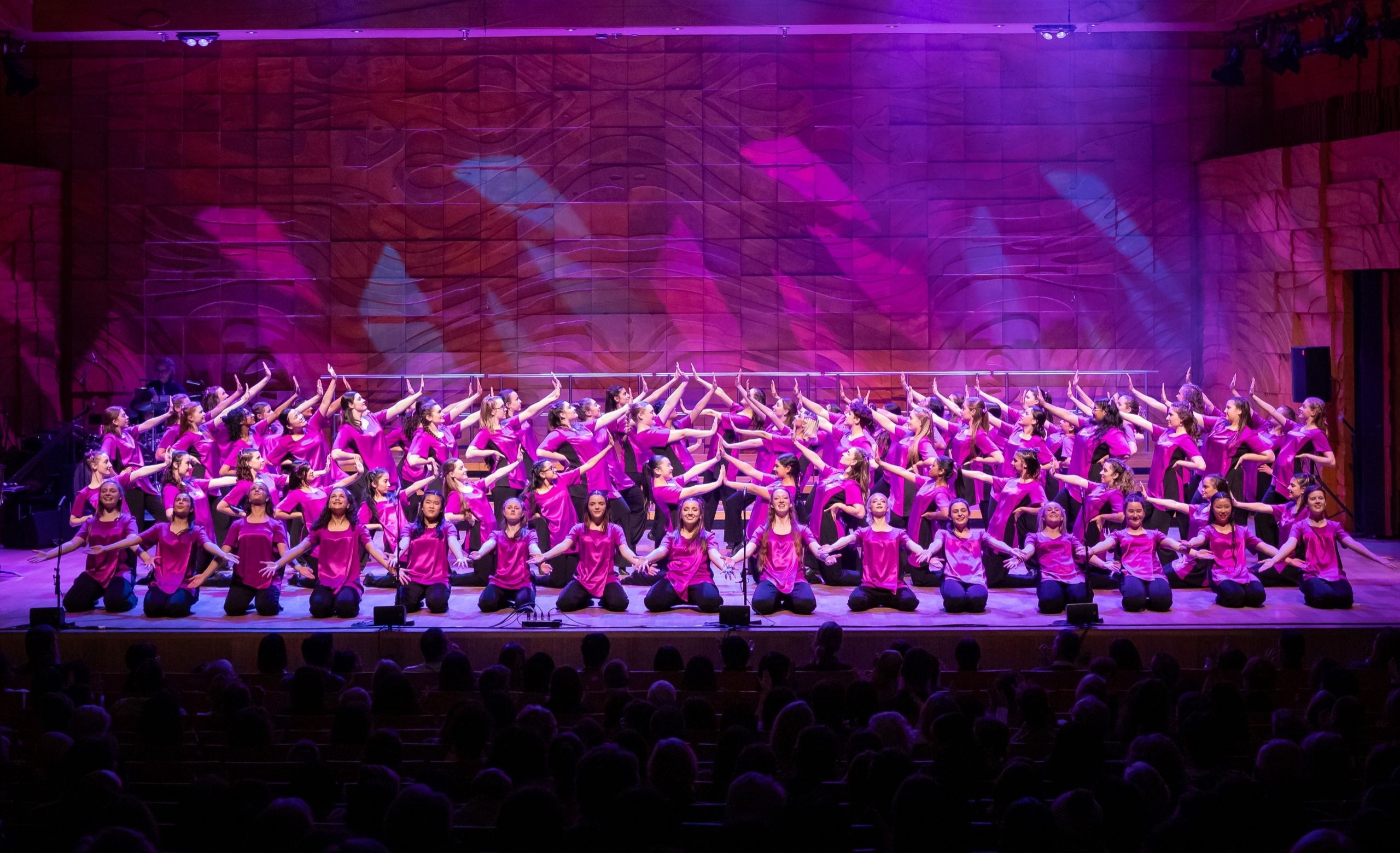 Big group shot of choristers holding final position on stage with their arms out.