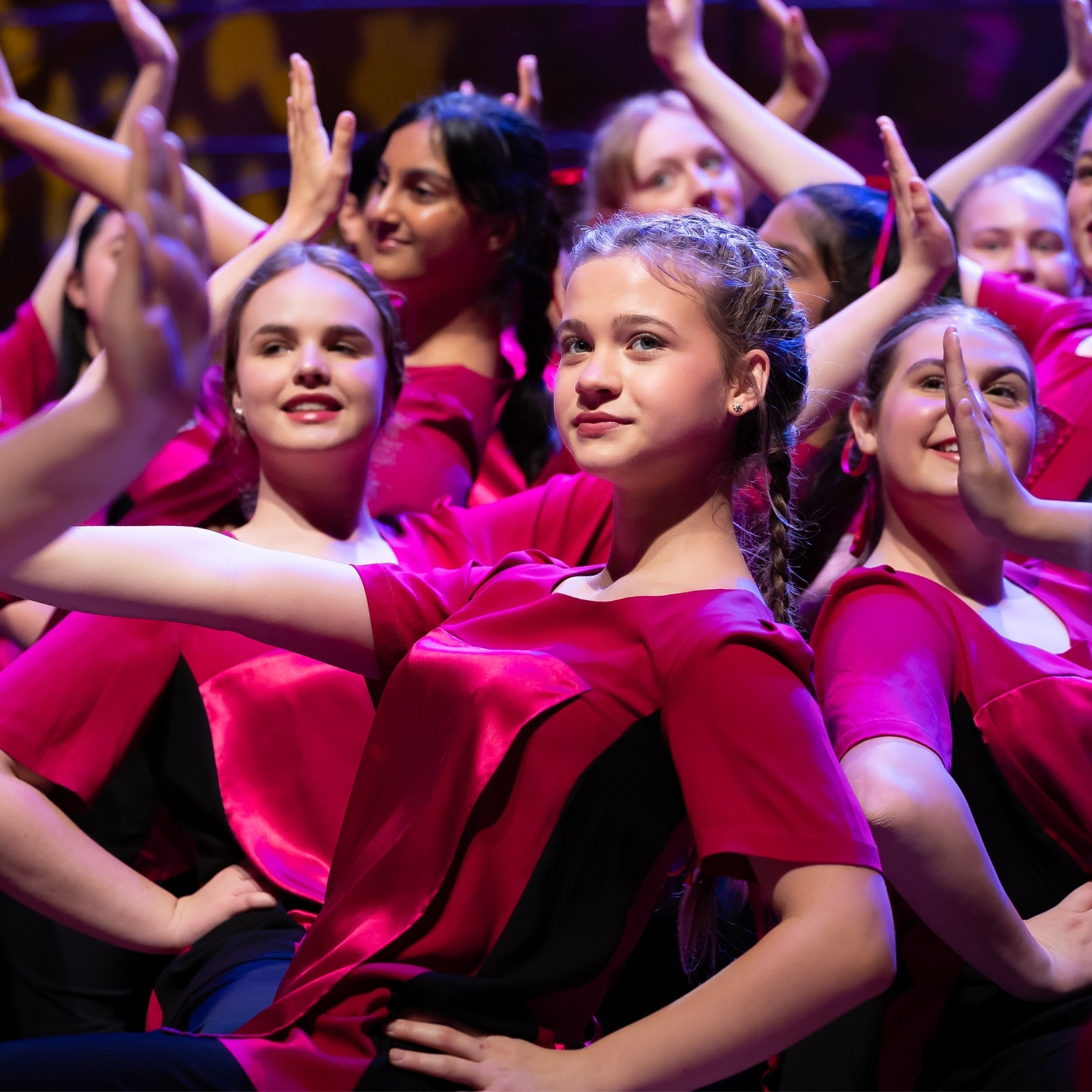 Camerata perform on stage during a concert in a big group number with their arms up