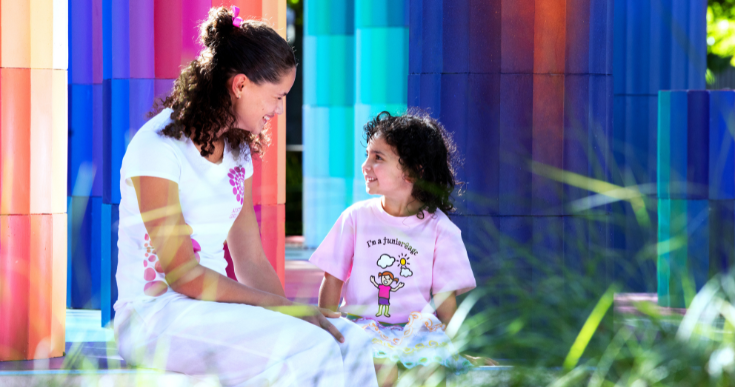 An AGC big girl and little girl laugh and smile together in a colourful setting.