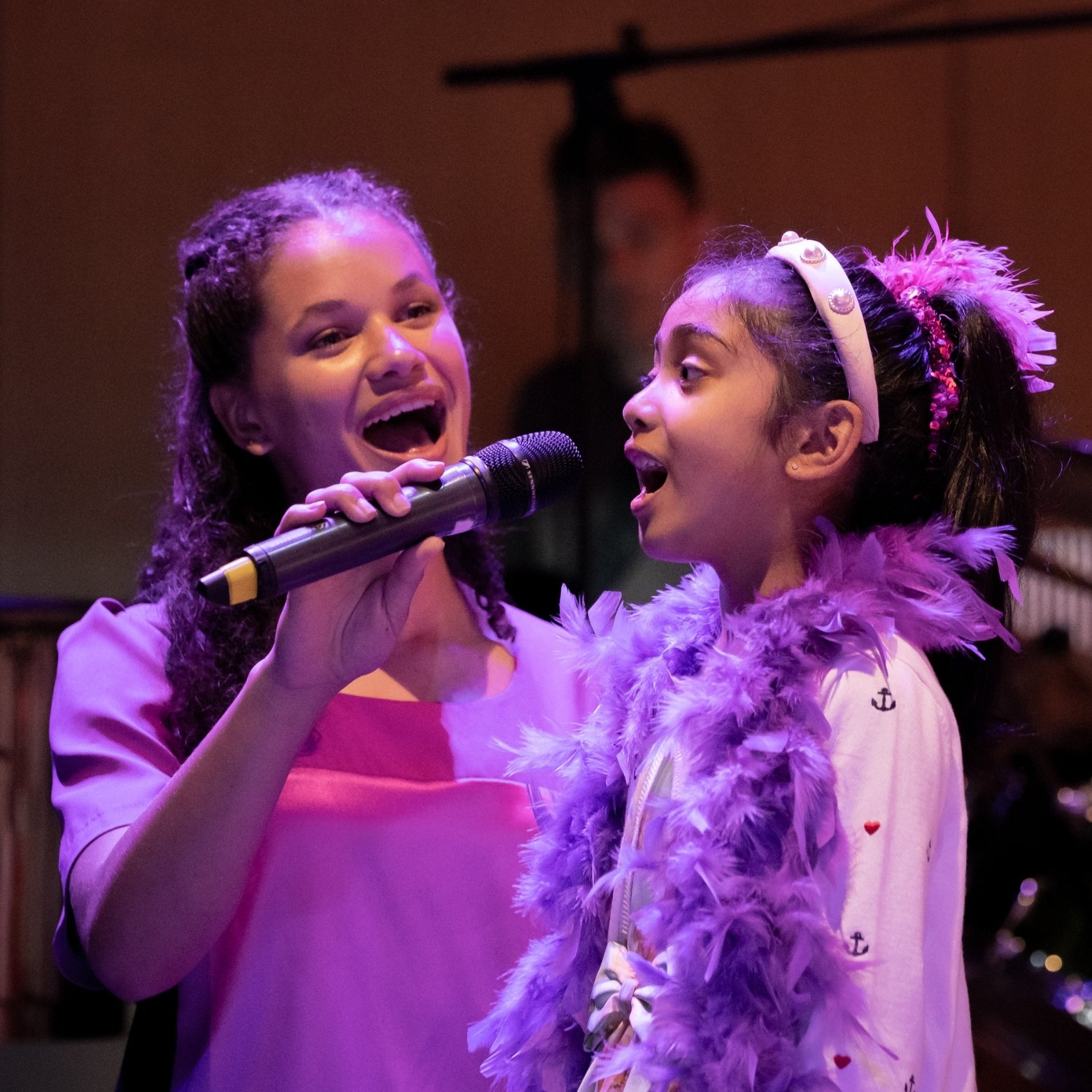 Older chorister holding microhpone for younger chorister during performance