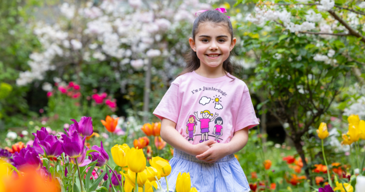 A junior@agc choristers stands in a beautiful flower garden