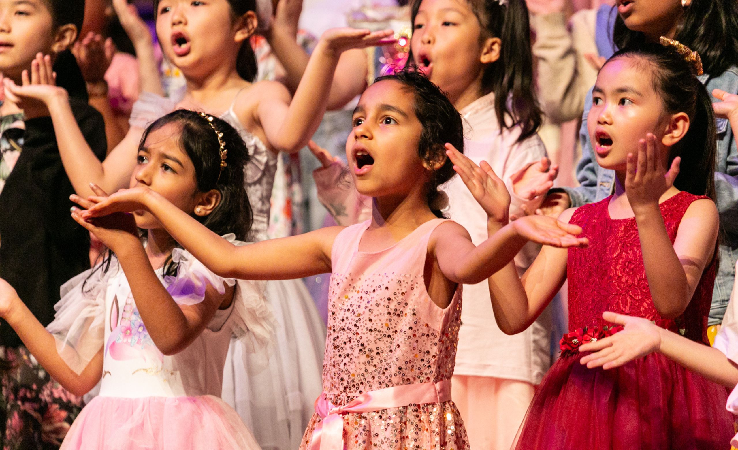 A junior@agc chorister throws her arms out on stage